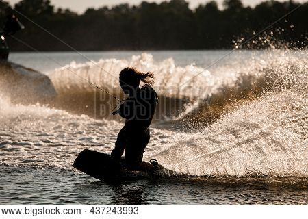 Wet Male Wakeboarder Holds Taut Rope And Trying To Stand On Splashing Wave.