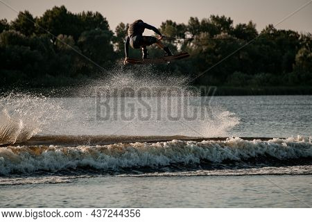 Wonderful View Of Dynamic Guy Holding Rope And Jumping High With Wakeboard Over Water