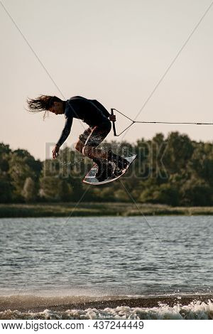 Active Man Holding Rope And Making Trick In Jump Time With Wakeboard Over Water