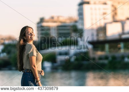 Young Cacucasian Woman Turning To The Camera During Sunset Next To Urban River