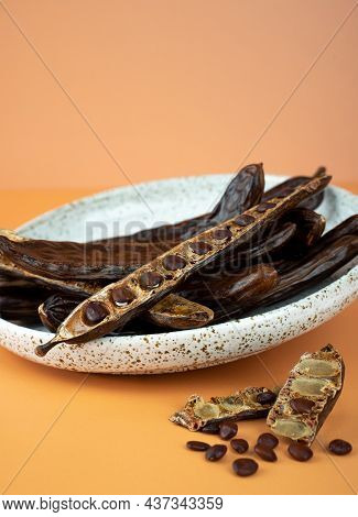 Organic Carob Pods, Seeds In A Ceramic Plate On A Beige Background, Locust Bean Healthy Food, Cerato
