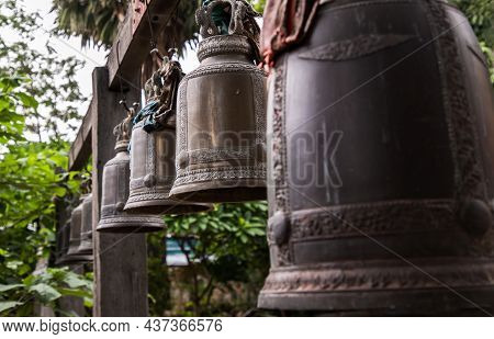 Many Metallic Bells Hanging In A Row On Wooden Pillars Outside In Thai Buddhist Temple. Lined With M