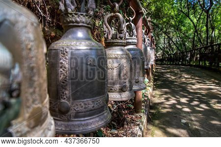 Many Metallic Bells Hanging In A Row On Wooden Pillars Outside In Thai Buddhist Temple. Lined With M