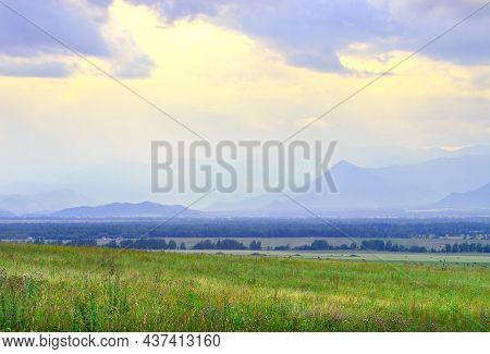 Grassy Steppe Among Blue Mountains In Fog, Cloudy Sunset Sky. Siberia, Russia