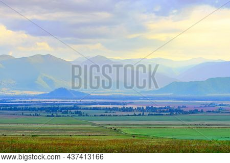 Grassy Steppe Among Blue Mountains In Fog, Cloudy Sunset Sky. Siberia, Russia