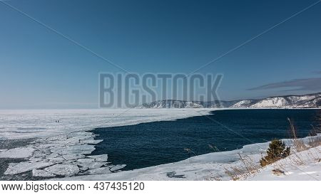 A Non-freezing River Flows Out Of A Frozen Lake. White Ice Floes On Blue Water. A Mountain Range Aga