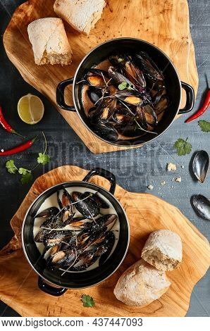 Mussel stew pot with creamy sauce, baguette on stone table. Mussels soup pot contemporary style. Aesthetic composition with seafood. Gastronomy mussel pot dinner concept. Stone table and wooden tray