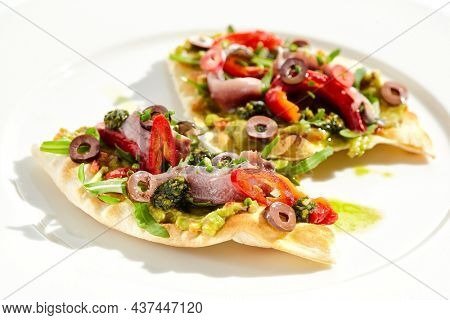 Tapas with avocado cream, anchovy, paprika and kalamata olives on focaccia. Bruschetta with guacamole and anchovy isolated on white background. Appetizer contemporary concept. Fish antipasti