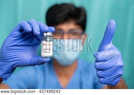 Doctor With Medical Face Showing Malaria Vaccine Bottle With Thumbs-up Gesture - Concept Of New Succ