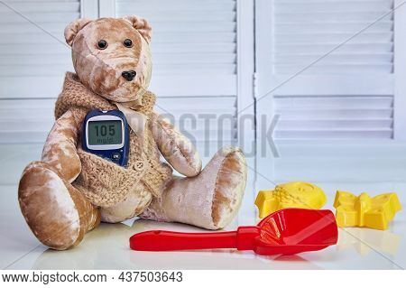 Teddy Bear With A Blood Glucose Meter And Scattered Children's Toys On A Blue Background. The Concep
