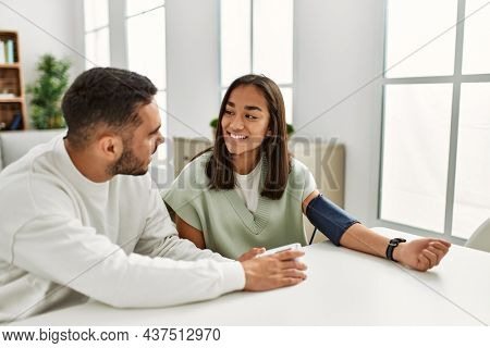 Young latin couple smiling happy measuring blood pressure using tensiometer at home.