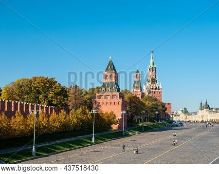 View Of The Kremlin From The Moskvoretsky Bridge Against The Blue Sky. People Walk Along Red Square.