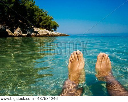 Feet Of A Man Floating In The Clear Azure Water In A Sunny Day