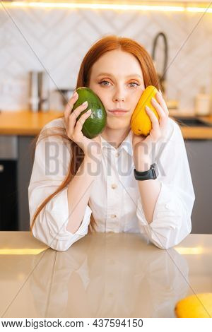 Vertical Portrait Of Serious Attractive Redhead Young Woman Holding In Hands Mango And Avocado Sitti