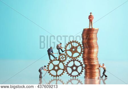 Miniature Businessman On Top Of A Pile Of Coins With Construction Workers, Leadership, Success Conce