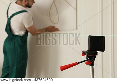 Cross Line Laser Level And Handyman Hanging Picture On White Wall