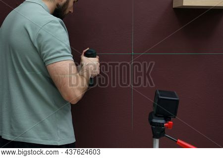 Man Using Cross Line Laser Level For Accurate Measurement And Drilling Hole In Brown Wall, Closeup