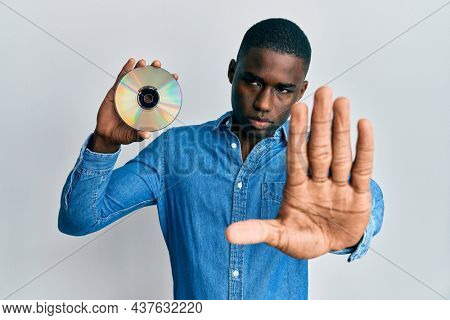 Young african american man holding compact disc with open hand doing stop sign with serious and confident expression, defense gesture 