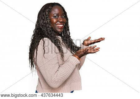Young african woman wearing wool winter sweater pointing aside with hands open palms showing copy space, presenting advertisement smiling excited happy 