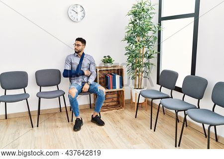 Young arab man sitting on chair with arm sling at clinic waiting room