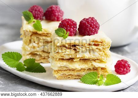Pieces Of Napoleon Cake Decorated With Raspberries And Lemon Balm Leaves On A Light Background.