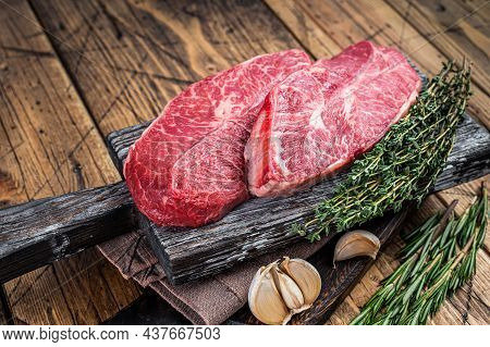Raw Shoulder Top Blade Beef Meat Steaks On A Wooden Butcher Board With Herbs. Wooden Background. Top