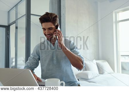 Caucasian man working remotely from home. Male uses laptop computer and smartphone. Idea of remote and freelance work. Young guy wearing casual formal clothes. Modern successful man lifestyle.