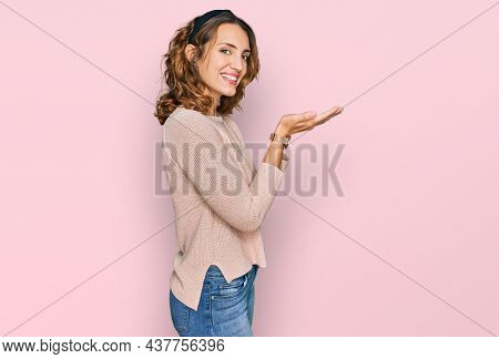 Beautiful young caucasian woman wearing casual sweater pointing aside with hands open palms showing copy space, presenting advertisement smiling excited happy 