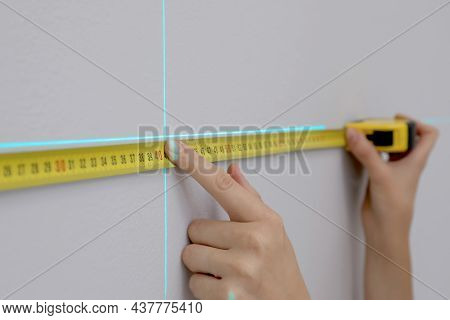 Woman Using Cross Line Laser Level And Tape For Accurate Measurement On Grey Wall, Closeup