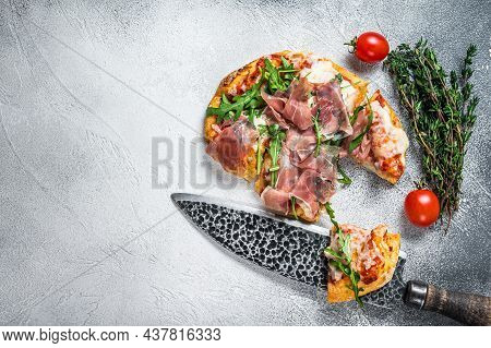 Italian Pizza With Parma Ham, Arugula And Cheeseon A Kitchen Table. White Background. Top View. Copy