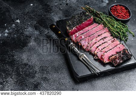 Rare Ahi Tuna Steak Slices With Fresh Herbs On A Cutting Board. Black Background. Top View. Copy Spa