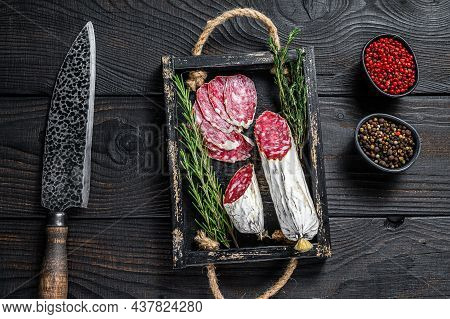 Slices Of Dry Cured Salchichon Salami In A Wooden Tray. Black Wooden Background. Top View