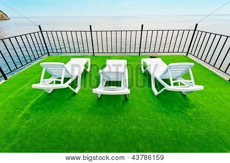 Trois blancs chaise longue plage sur un pont vert avec vue sur la mer.
