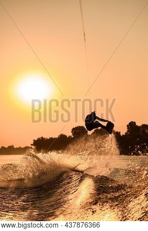 Active Man Making Trick With Wakeboard On Bright Orange Sky And Sun Background.