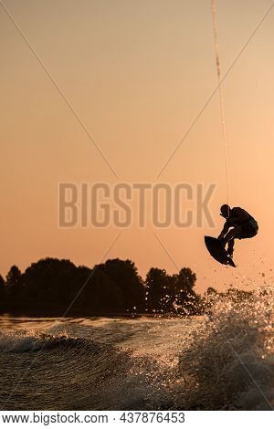 Great View Of Active Male Rider Holds Rope And Making Jump On Wakeboard At Evening Sky On Background