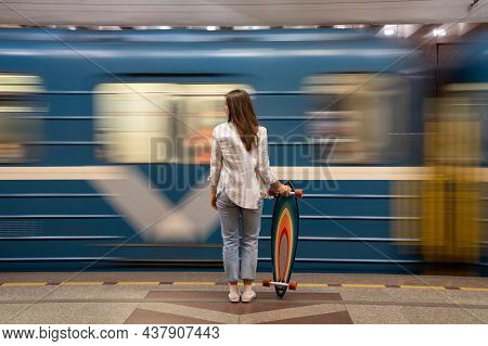 Young Girl Passenger With Longboard Standing On Subway Station Platform With Blurry Moving Blue Trai