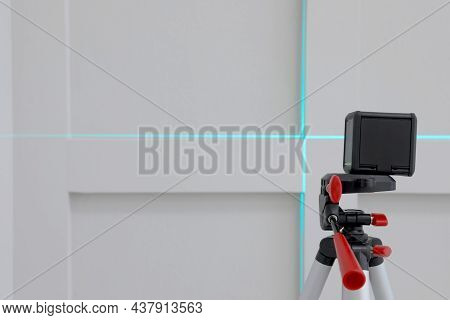 Cross Line Laser Level On Tripod In Front Of Light Wall