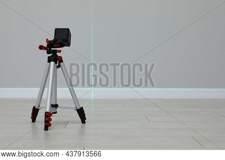 Cross Line Laser Level On Tripod In Front Of Light Wall Indoors