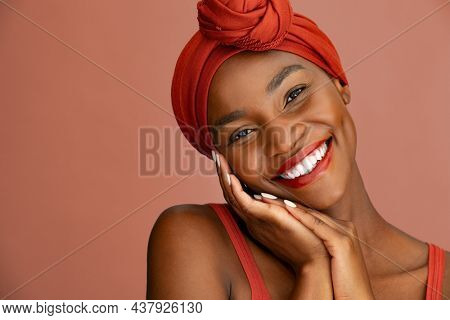 Portrait of beauty and lovely woman with ethnic headscarf looking at camera. Confident mid adult black woman smiling while wearing red headband against red wall. Beautiful african american mid woman.