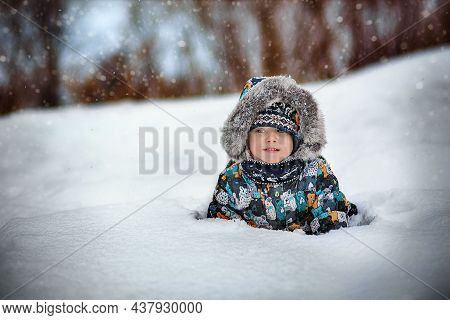 Cute Caucasian Boy In Warm Winther Jacker With Fur Hoody Laying In Snow In Countryside On Winter Day