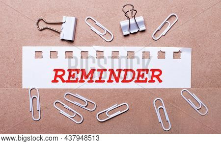On A Brown Background, White Paper Clips And A Torn Strip Of White Paper With The Text Reminder