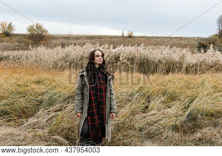 Young Dreamy Thoughtful Woman Wearing Grey Old Fashioned Coat Stands In Dry Grass Reeds Field Lookin