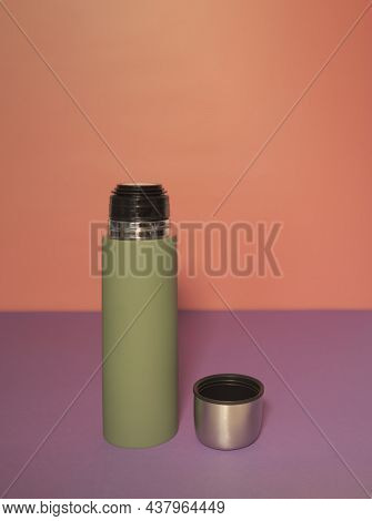 Green Thermos With Open Lid On A Peach-fiolet Background