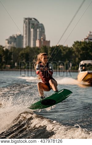 Beautiful Active Woman Holds Rope And Jumping With Wakeboard Over River Wave.