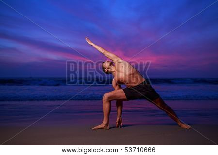 Man in stretching yoga pose on ocean beach at dusk