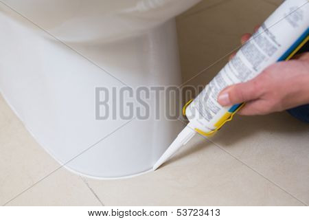 Close up of a plumber fixing toilet in a washroom with silicone cartridge