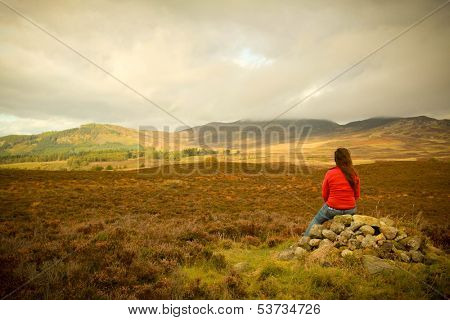 Woman sit on a pile of stones and look at the mountains from Cairngorms in Scotland