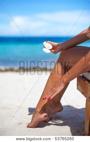 Young Woman Apply Cream On Her Smooth Tanned Legs At Tropical Beac