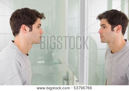 Side view of a tensed young man looking at self in mirror in the bathroom