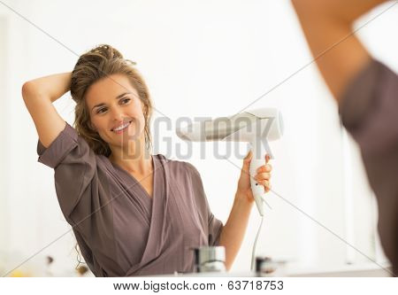 Happy Young Woman Blow Drying Hair In Bathroom
